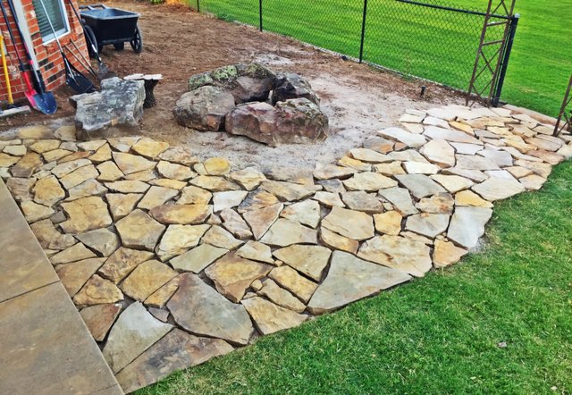 Finished flagstone patio wrapping around a boulder fire pit on a gravel pad