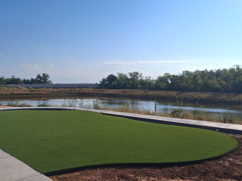 After: the same pad finished as an artificial turf lawn beside the pond