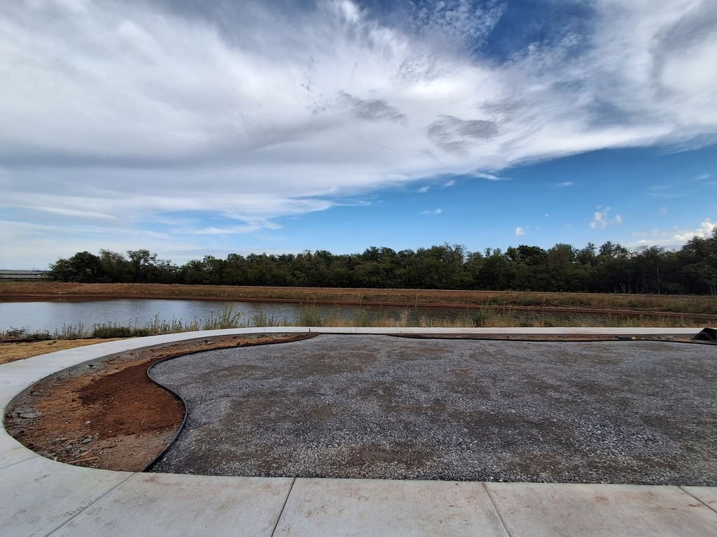 Before: compacted gravel base inside black edging on a pond-side lot