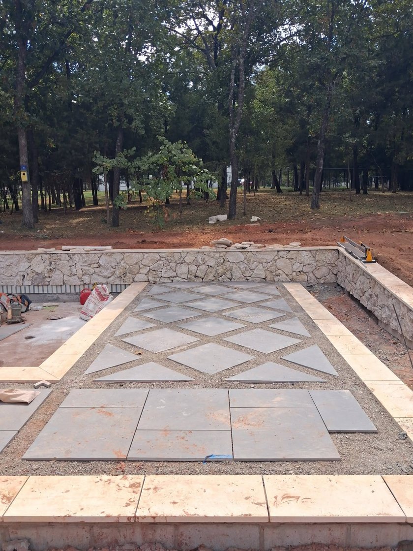 Large gray pavers set on the diagonal in pea gravel beside a pool, framed by a stacked stone retaining wall