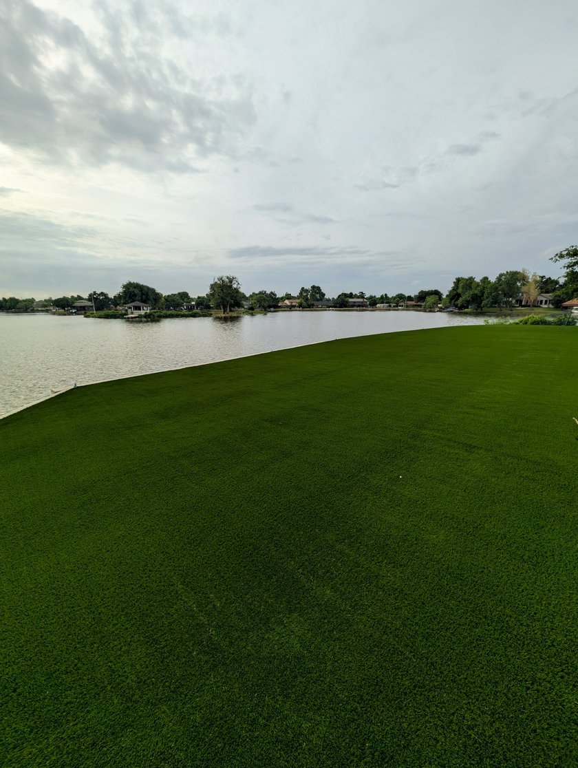 Artificial turf lawn running to the edge of a lake behind a home