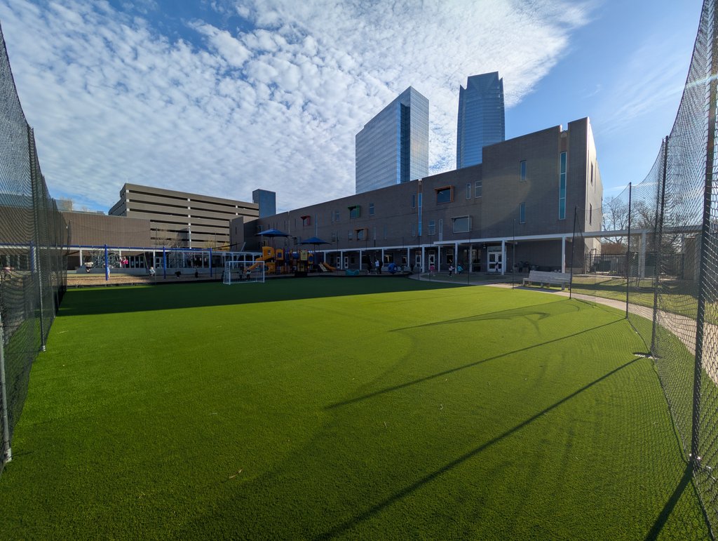 Fenced artificial turf play field with a soccer goal next to a downtown Oklahoma City school