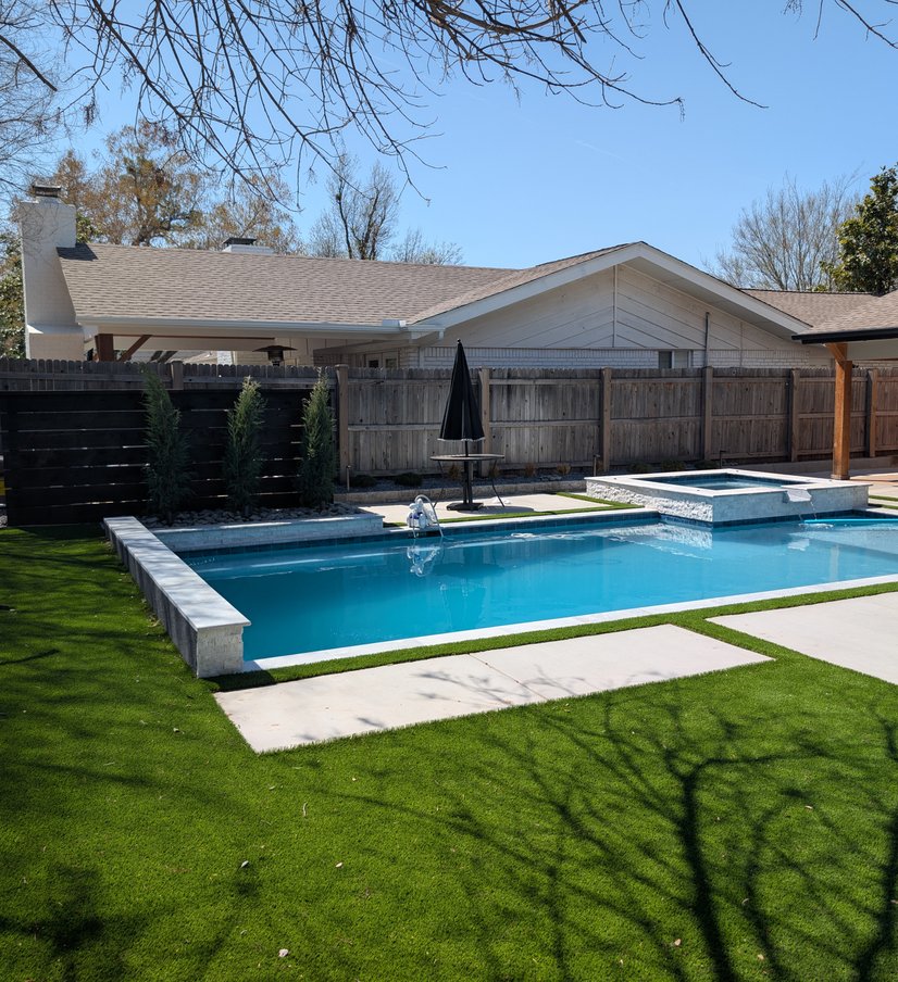 Finished backyard pool with a raised spa, concrete deck and artificial turf lawn