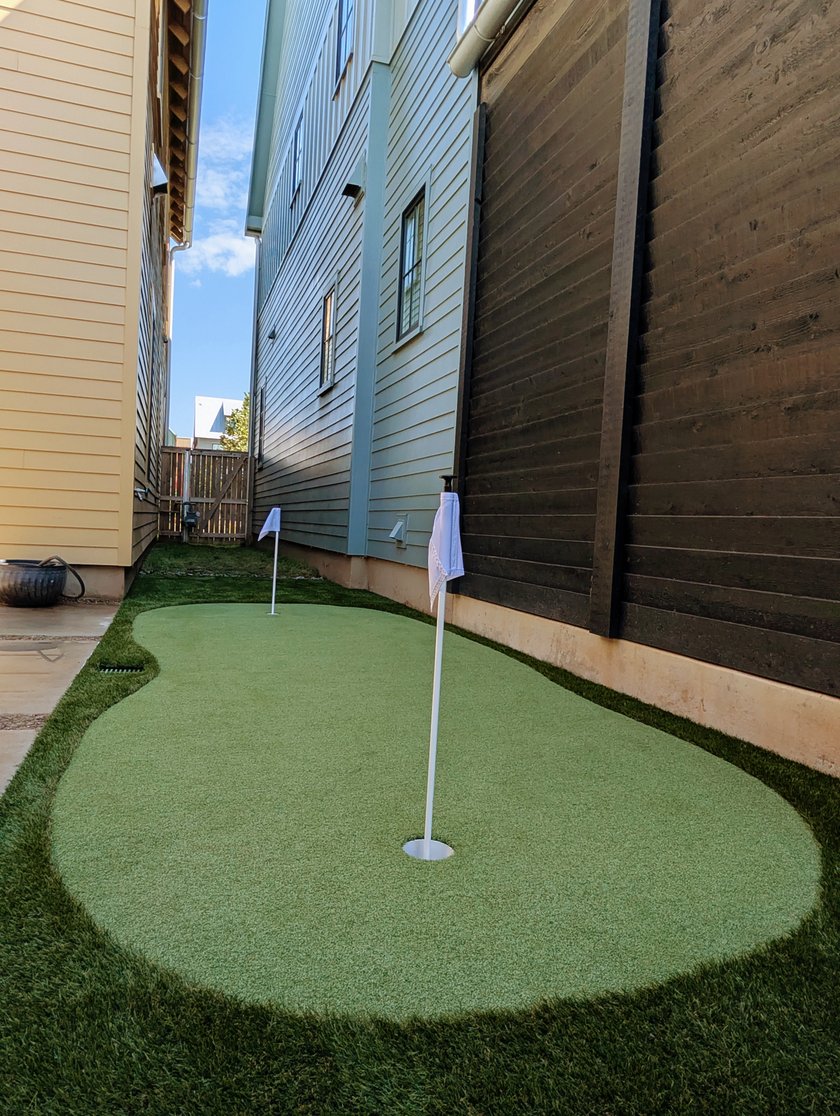 Two-cup artificial putting green built into a narrow side yard between two houses