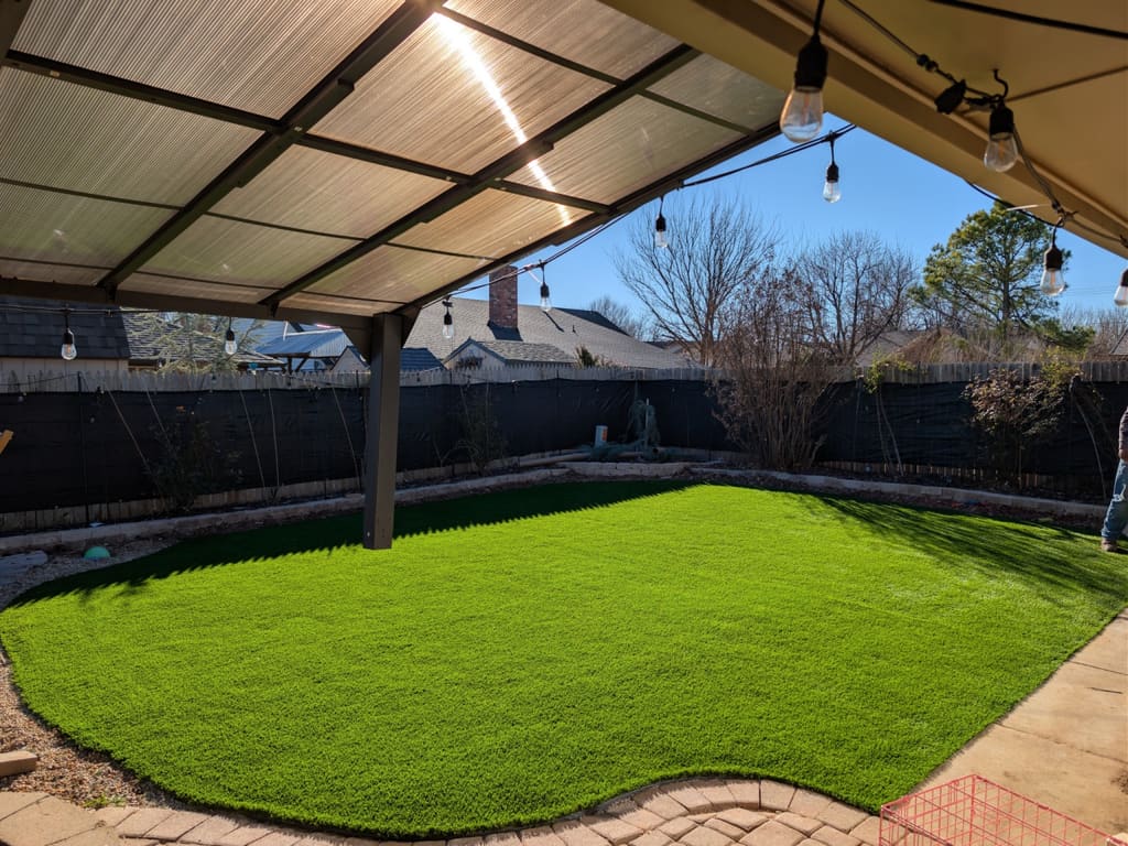After: artificial turf lawn curving along the same paver patio under the covered pergola