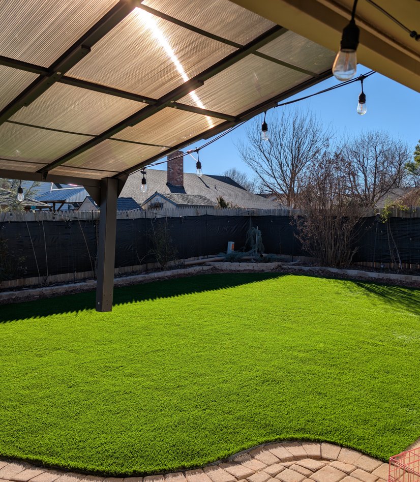 After: artificial turf lawn curving along the same paver patio under the covered pergola