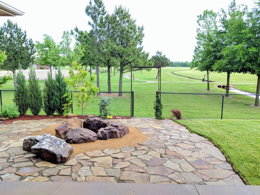 Flagstone patio with a boulder fire pit ring, evergreens and a metal arbor overlooking a golf course