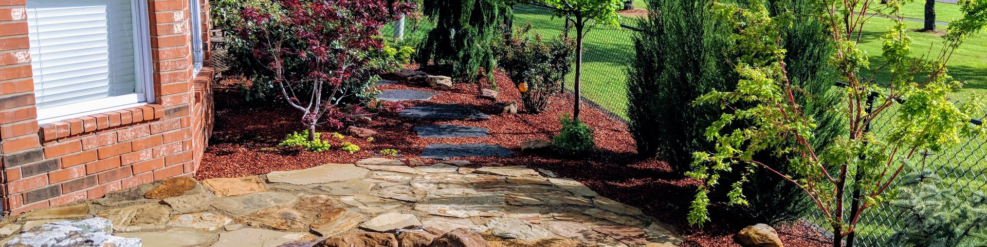 Flagstone patio with a boulder fire pit beside new landscape beds and Japanese maples