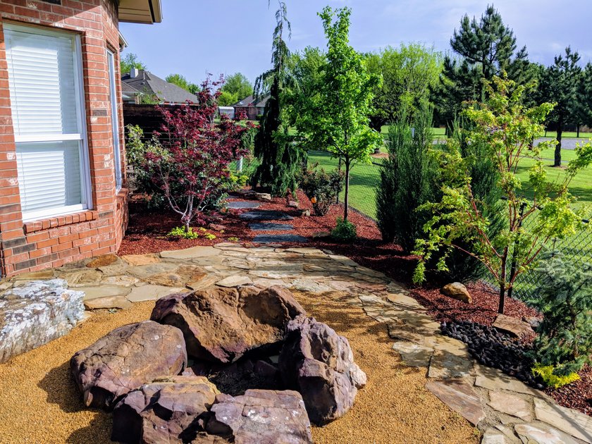 Flagstone patio with a boulder fire pit, bordered by red mulch beds, Japanese maples and evergreens