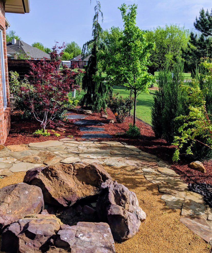 Flagstone patio with a boulder fire pit, bordered by red mulch beds, Japanese maples and evergreens