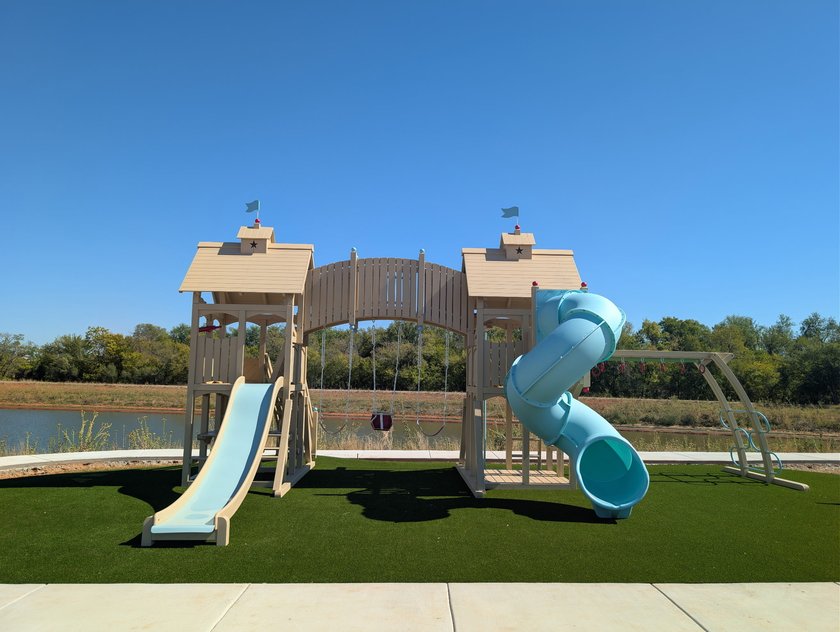 Playground with two towers, a spiral slide and swings set on artificial turf beside a pond