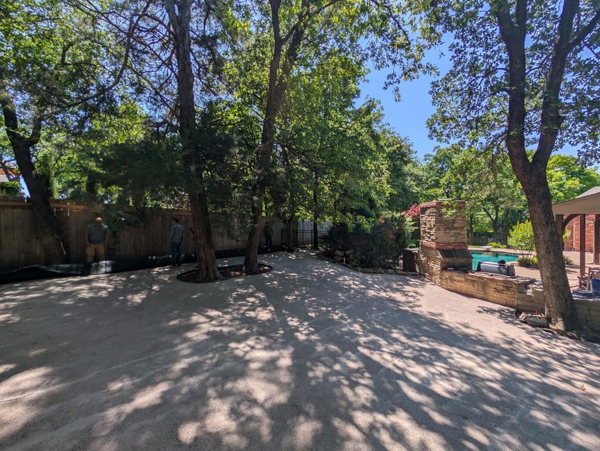 Compacted gravel base graded under shade trees, ready for a pet turf install