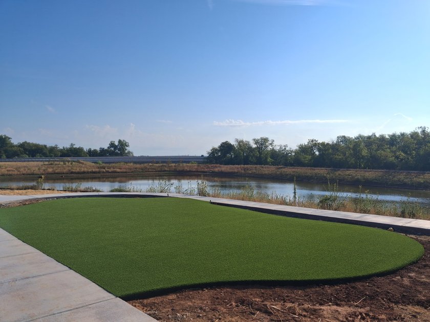 Artificial turf lawn beside a pond at a new development, edged by a concrete walk