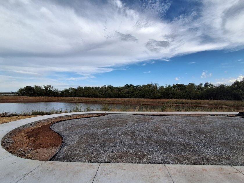 Compacted gravel base inside black edging on a pond-side lot, ready for turf