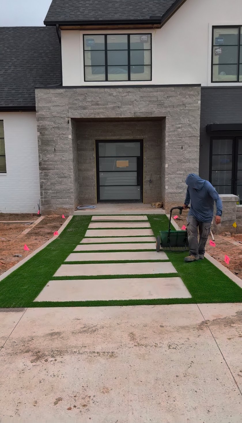 Installer spreading antimicrobial sand infill over turf between walkway pavers at a front entry