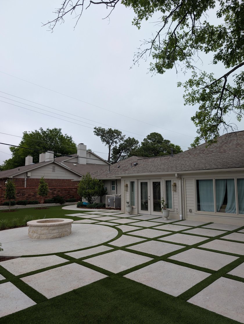 Concrete paver patio with artificial turf strips curving around a round stone fire pit