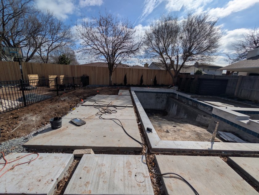 Large concrete pavers set on bare ground around a new pool shell, before the turf goes in