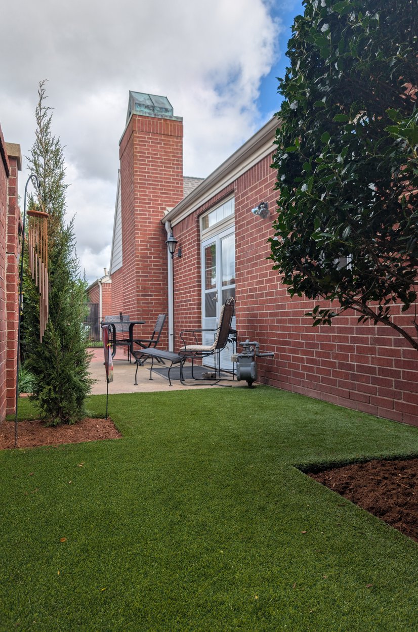 Artificial turf side yard running between a brick house and a fence to a small patio