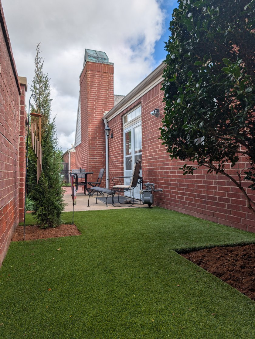Artificial turf side yard running between a brick house and a fence to a small patio